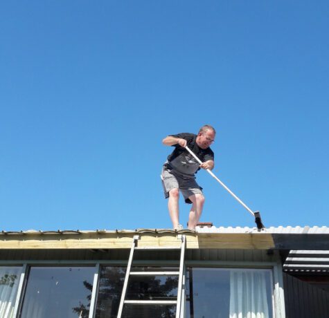 Homme nettoyant un toit en journée ensoleillée.