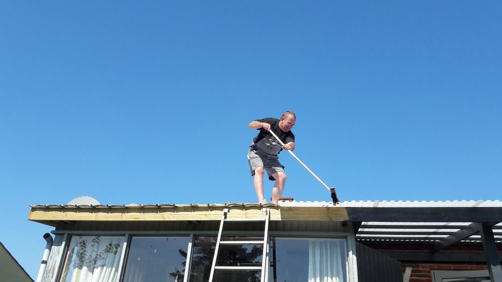 Homme nettoyant un toit en journée ensoleillée.
