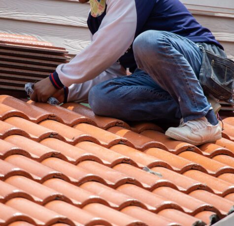 Travailleur inspectant toiture en tuiles orange sur bâtiment.