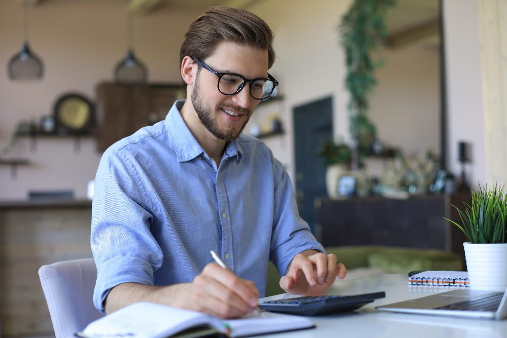Homme souriant calculant à un bureau moderne.