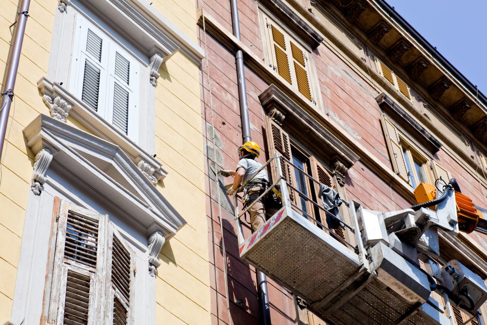 Travailleur rénove façade immeuble sur nacelle élévatrice.